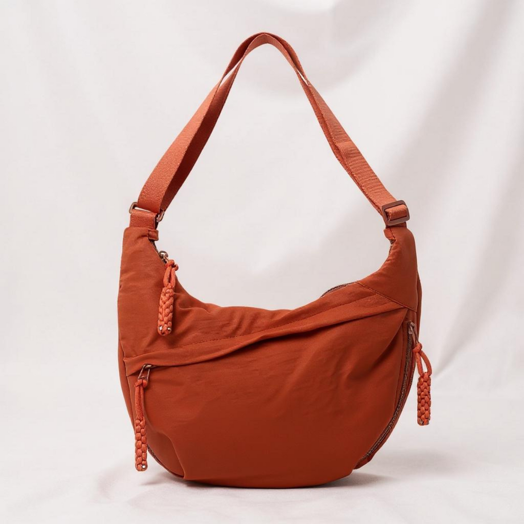 Rust orange crescent shoulder bag with a matching adjustable strap and braided zipper pulls, another view.