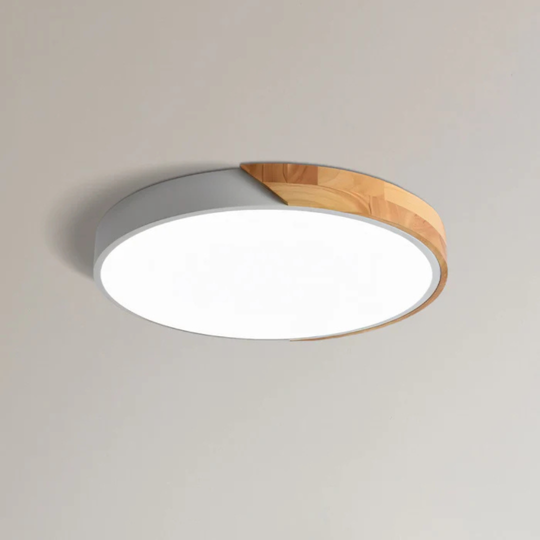 Round flush-mount ceiling light switched on, seen from below, with a light gray side band partly covered by a natural wood segment. 21