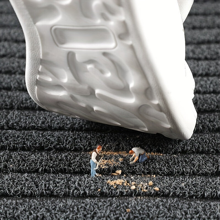 Grey striped doormat detail with a sneaker sole above the looped surface and crumbs of dirt caught in the loops.