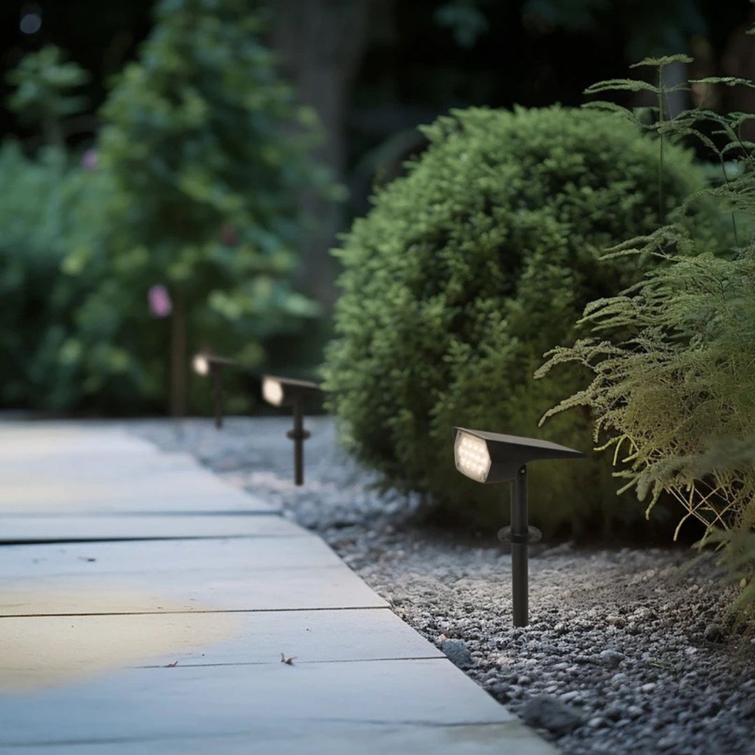 Three black solar spotlights glowing along a gravel strip beside a paved walkway.