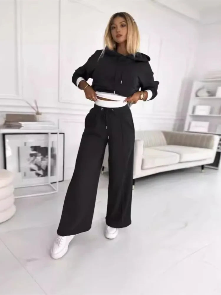 Model in a black cropped hoodie and wide-leg drawstring pants, lifting the hem to show white trim 6