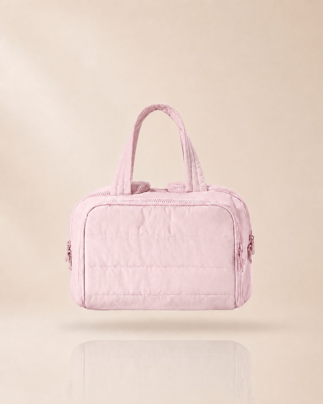 Pink quilted bag with handles raised, front view against a soft beige background with a faint reflection.