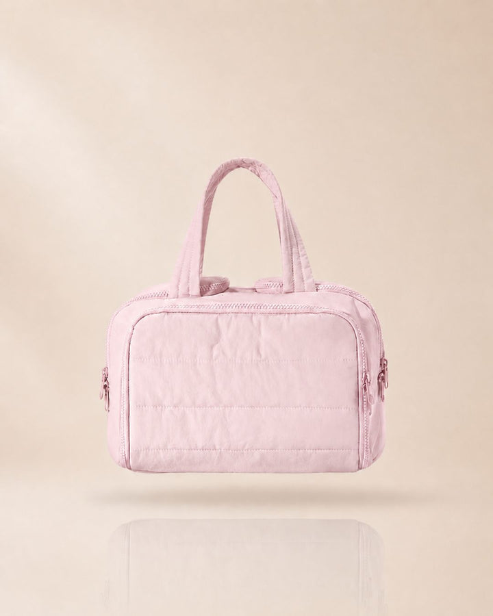 Pink quilted bag with handles raised, front view against a soft beige background with a faint reflection.