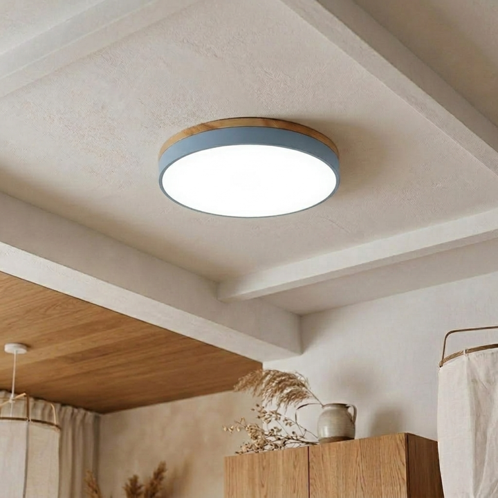 Light blue disc ceiling light with wood-grain trim shining bright cool white on a beamed plaster ceiling. 19