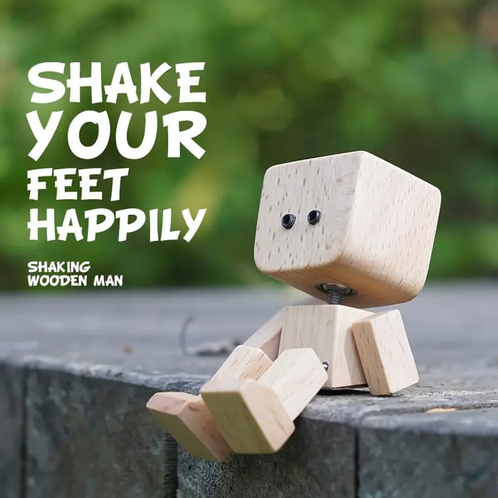 Wooden figure with round dot eyes sits on a stone ledge outdoors, feet dangling over the edge 13