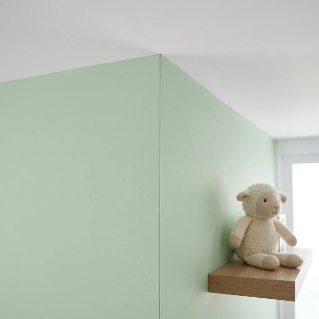 Pale green walls meeting a white ceiling in a sharp corner line, with a knitted lamb toy on a wooden shelf. 5