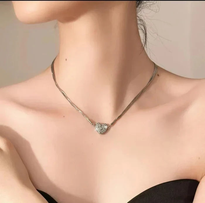 Side-angle view of the multi-strand silver necklace with a rhinestone heart worn on the collarbones of a woman in a strapless black top. 3