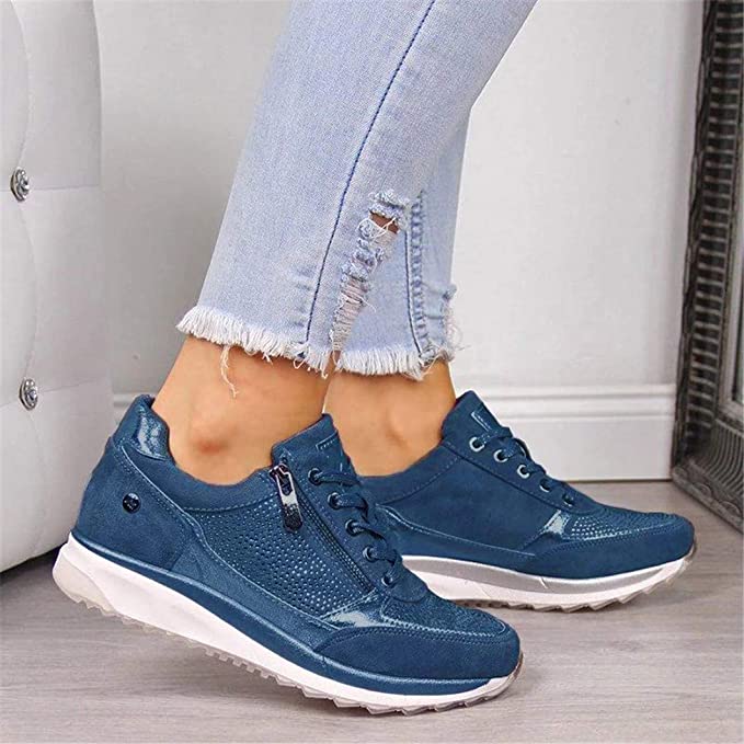 Another view of blue lace-up sneakers with a side zipper and studded panel, worn with light jeans.