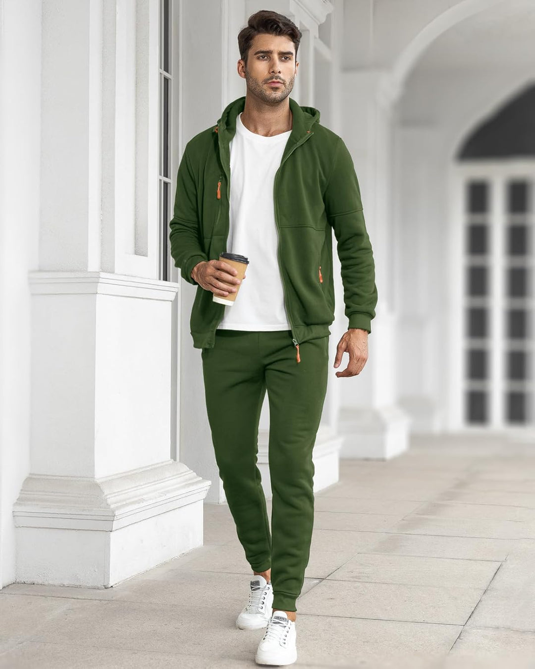 Model in the open olive green hoodie over a white tee and joggers, holding a coffee cup 19