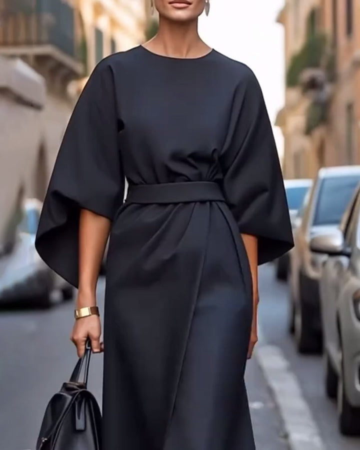 Front view of a black belted dress with wide flared sleeves and a gold cuff bracelet 5