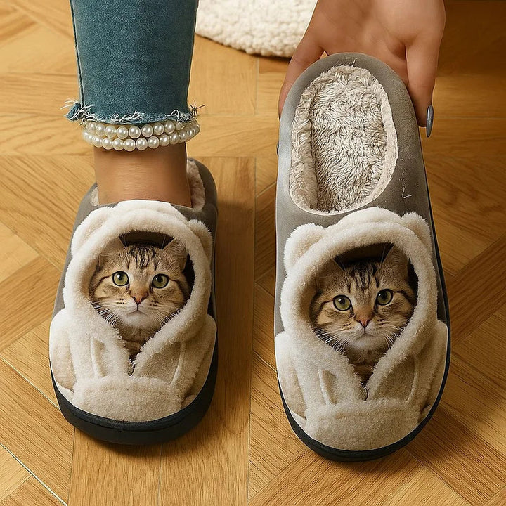 Gray slippers printed with a tabby cat in a fluffy hooded robe, one worn and one held up to show the plush lining. 1