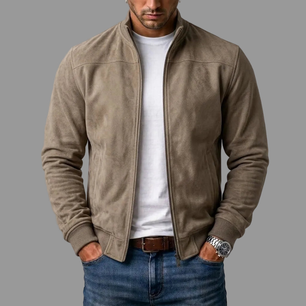 Taupe bomber jacket worn unzipped over a white tee, jeans and brown belt, with hands in pockets.