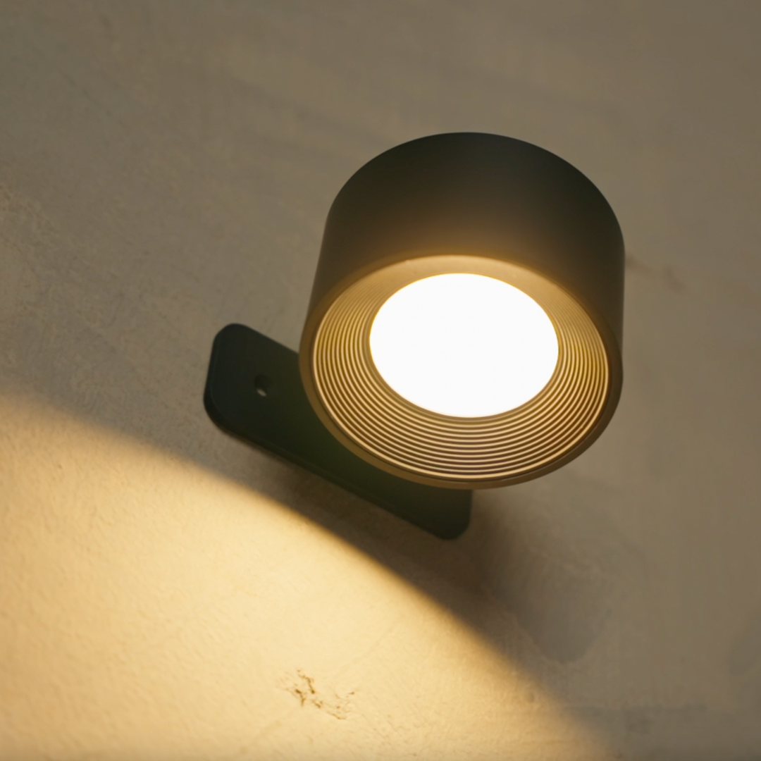 Close-up of the black wall light from below, glowing with a bright LED and showing the ribbed inner shade and mounting plate.