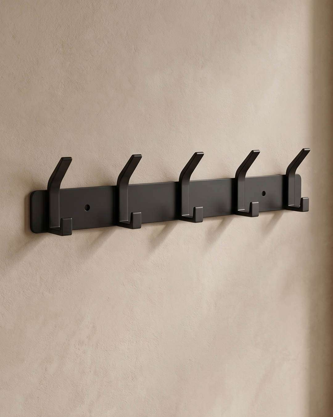 Black five-hook rack mounted straight-on against a beige plaster wall with two screw holes visible.