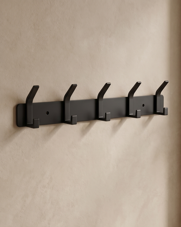 Black five-hook rack mounted straight-on against a beige plaster wall with two screw holes visible.