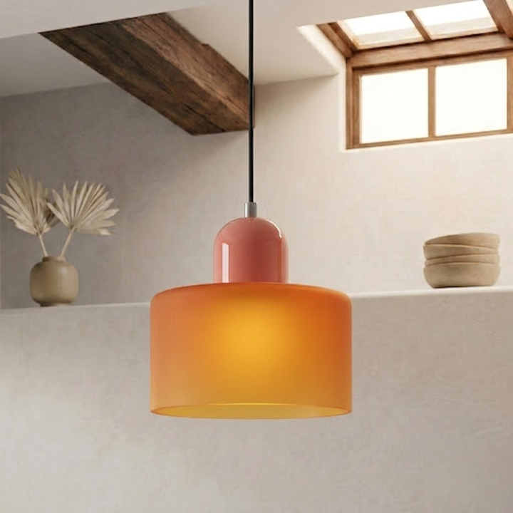Frosted amber-orange drum shade glowing warmly, with a coral-pink cap and black cord, in a plastered room. 13
