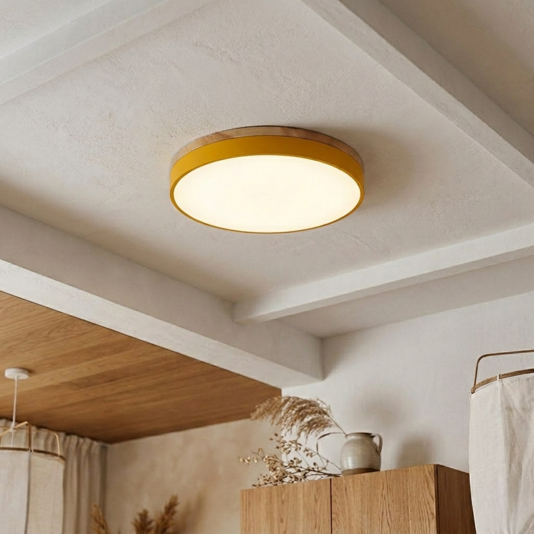 Yellow disc ceiling light with a wood-grain top band glowing warm white on a beamed plaster ceiling. 15