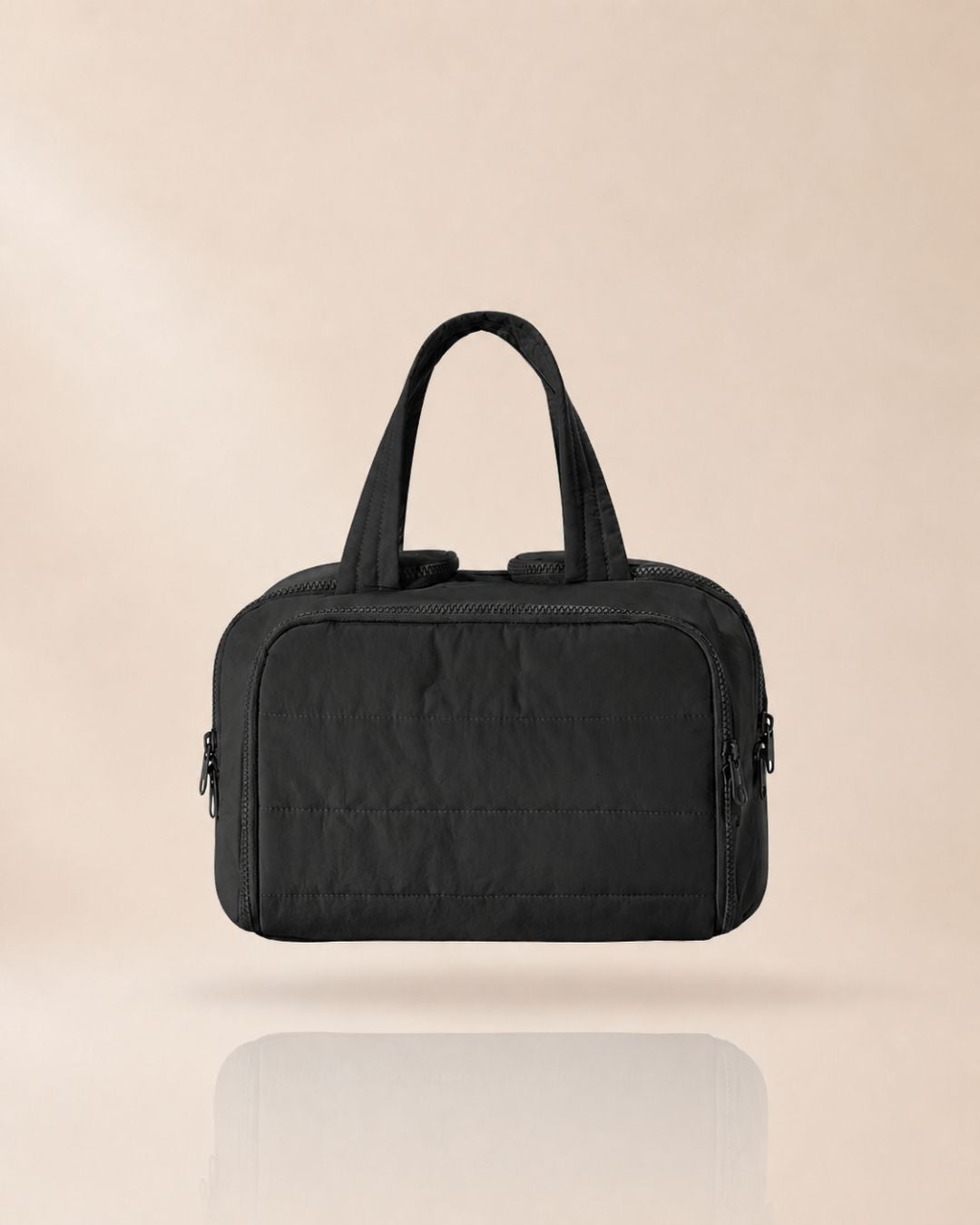 Black quilted bag with two handles, front view against a soft beige background.