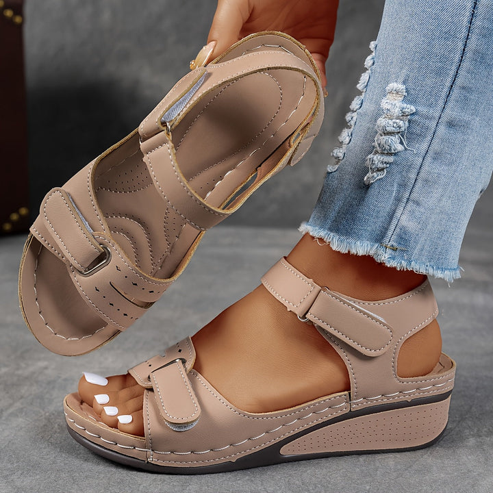 Beige wedge sandal with hook-and-loop straps, with the stitched, cushioned footbed visible. 7