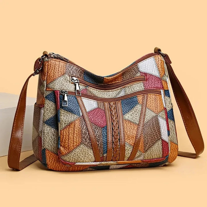 Front three-quarter view on a peach background of the patchwork bag with its braided trim, zip pockets and side pocket. 5