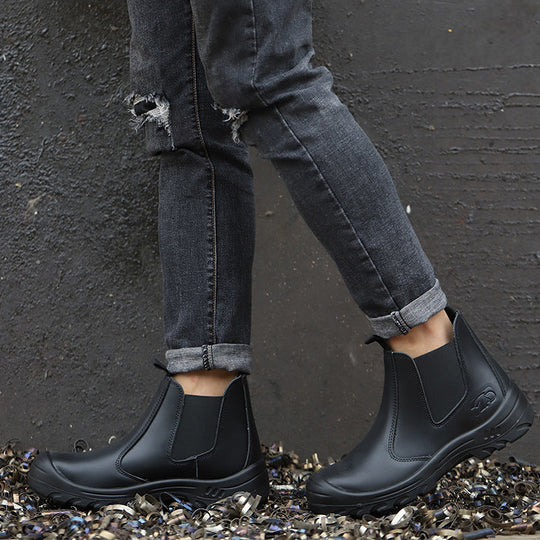 Model in gray jeans wearing black pull-on boots, standing on a bed of metal shavings against a dark wall 7