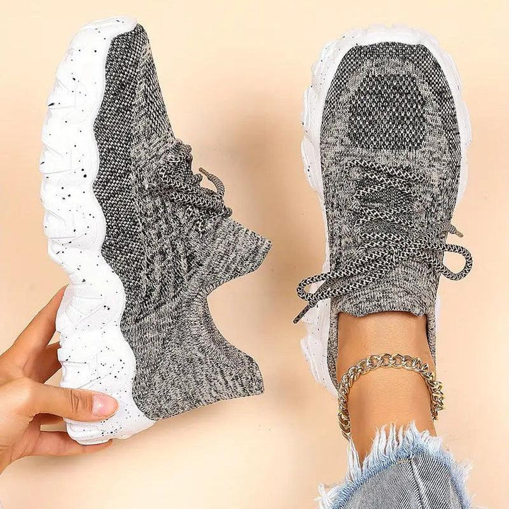 Top-down view of gray marled knit sneakers with white speckled soles, one held in hand and one worn with a gold anklet. 38