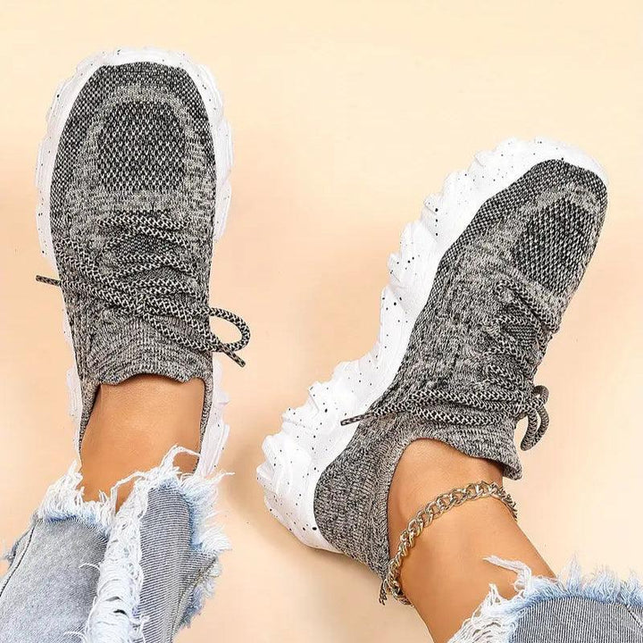 Top-down view of a model's feet in heathered gray knit lace-up sneakers with white speckled chunky soles and ripped jeans. 41