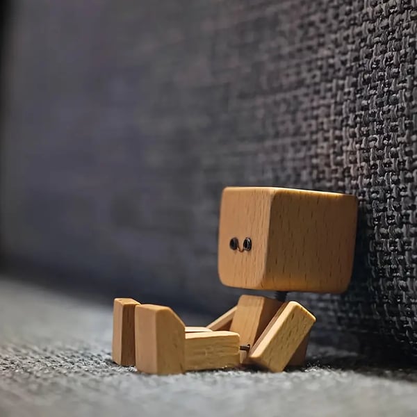 Wooden figure leans against a gray woven fabric wall, its legs stretched out in front 7