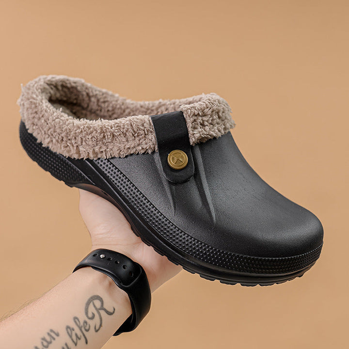 Hand holding a black fur-lined clog against a tan background, showing the side profile 2