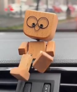 Close-up of wooden figure with ring eyes on a dashboard, one leg hanging over the vent 6