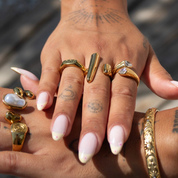 Axis adjustable sculptural gold ring worn on a hand with other gold rings and a bangle.