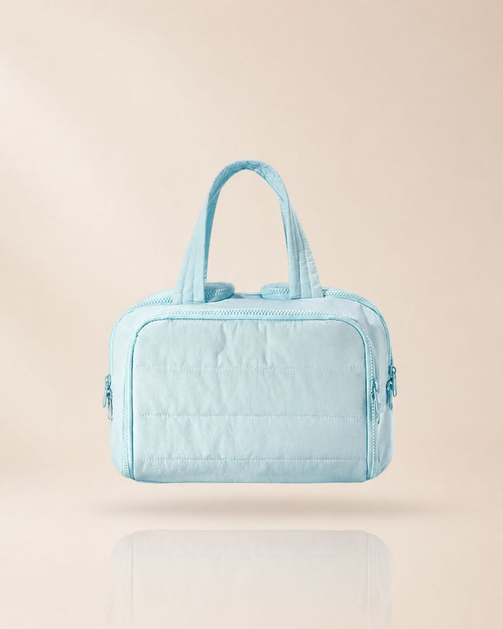 Light blue quilted bag with two handles, front view against a soft beige background.