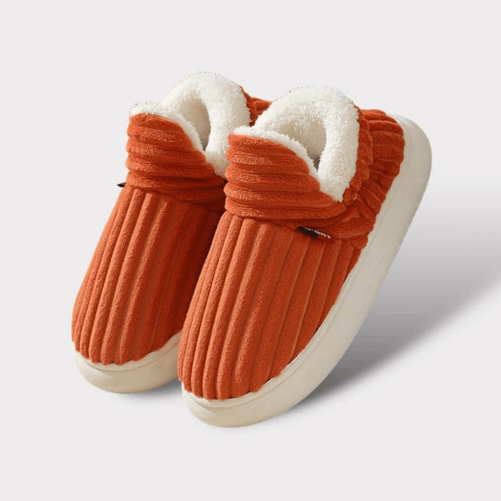 Pair of orange ribbed slippers with fluffy white fleece lining and thick cream soles on a plain light background.