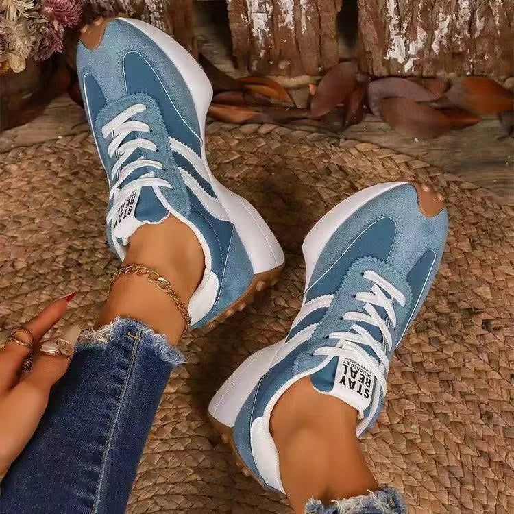 Top-down view of blue trainers with white stripes worn on a woven mat, with a gold ankle chain 8
