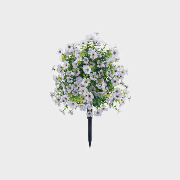 White artificial flower bush with light green leaves on a black ground stake against a plain gray background.