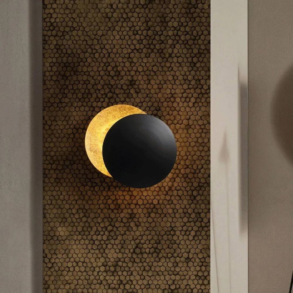Black disc lamp with golden crescent glow, mounted on a honeycomb-patterned wall panel 2