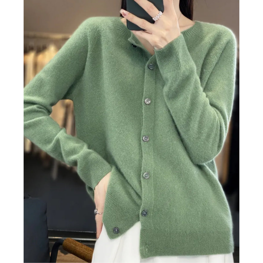 Woman in a sage green knit cardigan with dark buttons, taking a mirror selfie, hand on hip, styled with a white skirt. 13