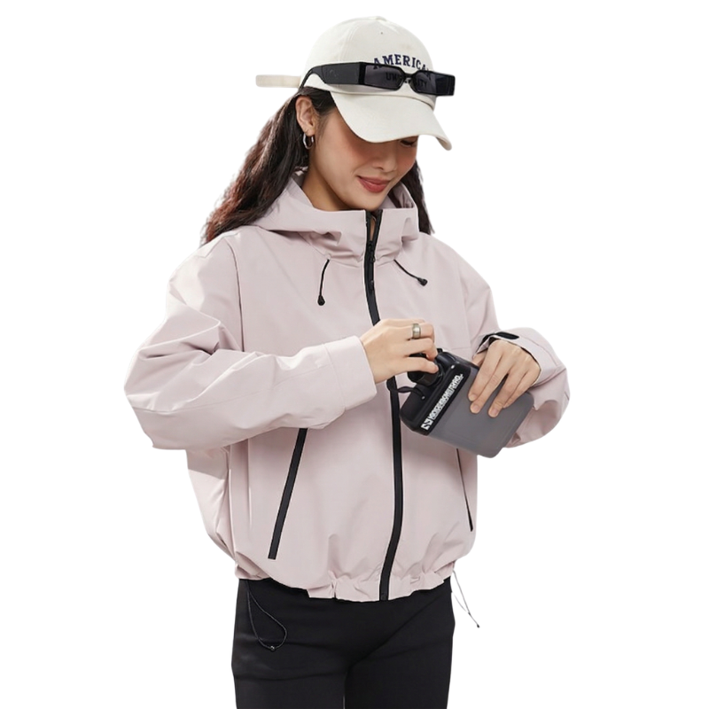 Model in the pink jacket checking a small black device held in both hands, hem drawcord cinched at the waist. 13