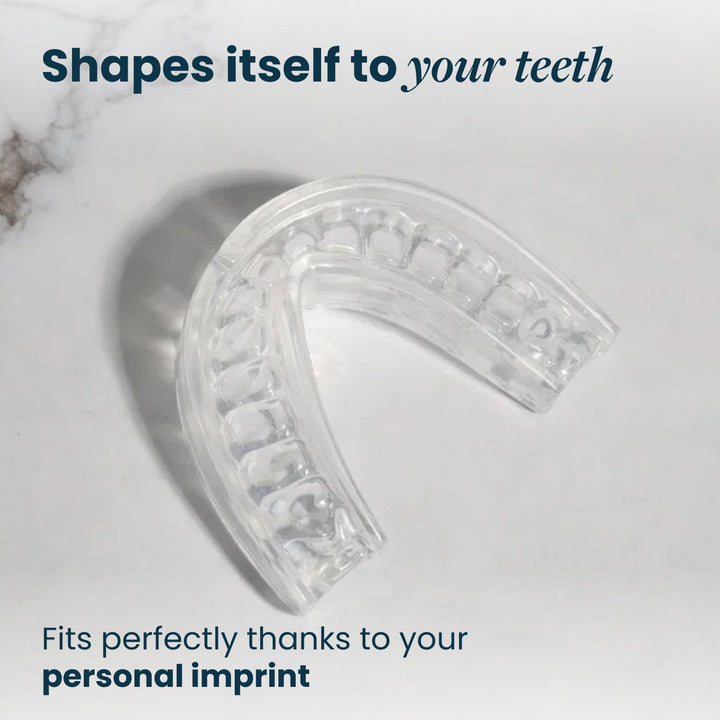 Top-down view of the clear mouthpiece showing the tooth-shaped impressions in its tray on a light marble surface. 28