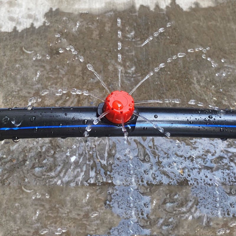 Red adjustable dripper on black tubing spraying thin streams of water outward.