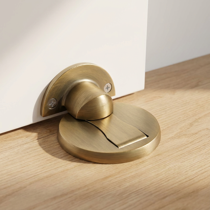 Antique brass door stopper in a lifestyle shot, door plate screwed to a white door and floor base on warm oak flooring. 7