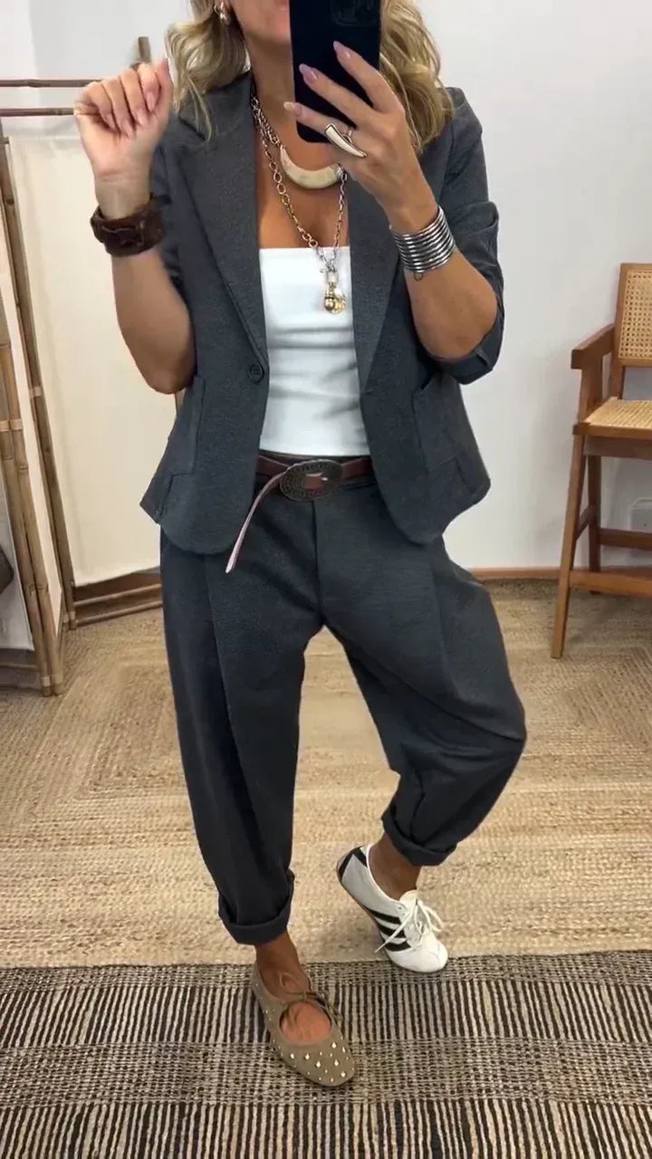 Dark gray suit set with a blazer and pleated pants, styled with a white top and brown belt.