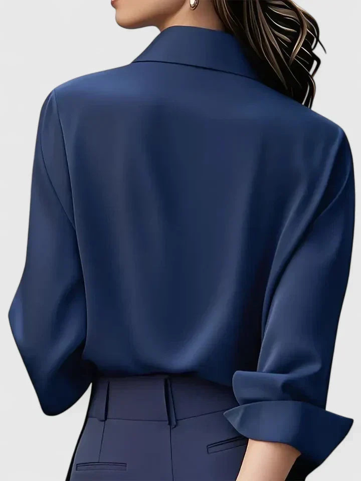 Back view of the navy blouse on a model, showing the smooth drape, collar and folded cuff.