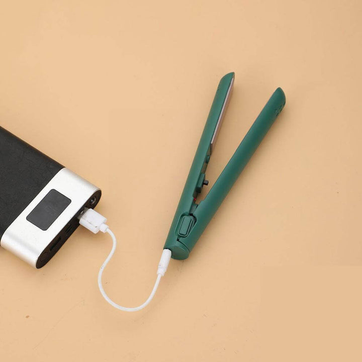 Green mini straightener opened and plugged by a white cable into a power bank on a peach surface 1