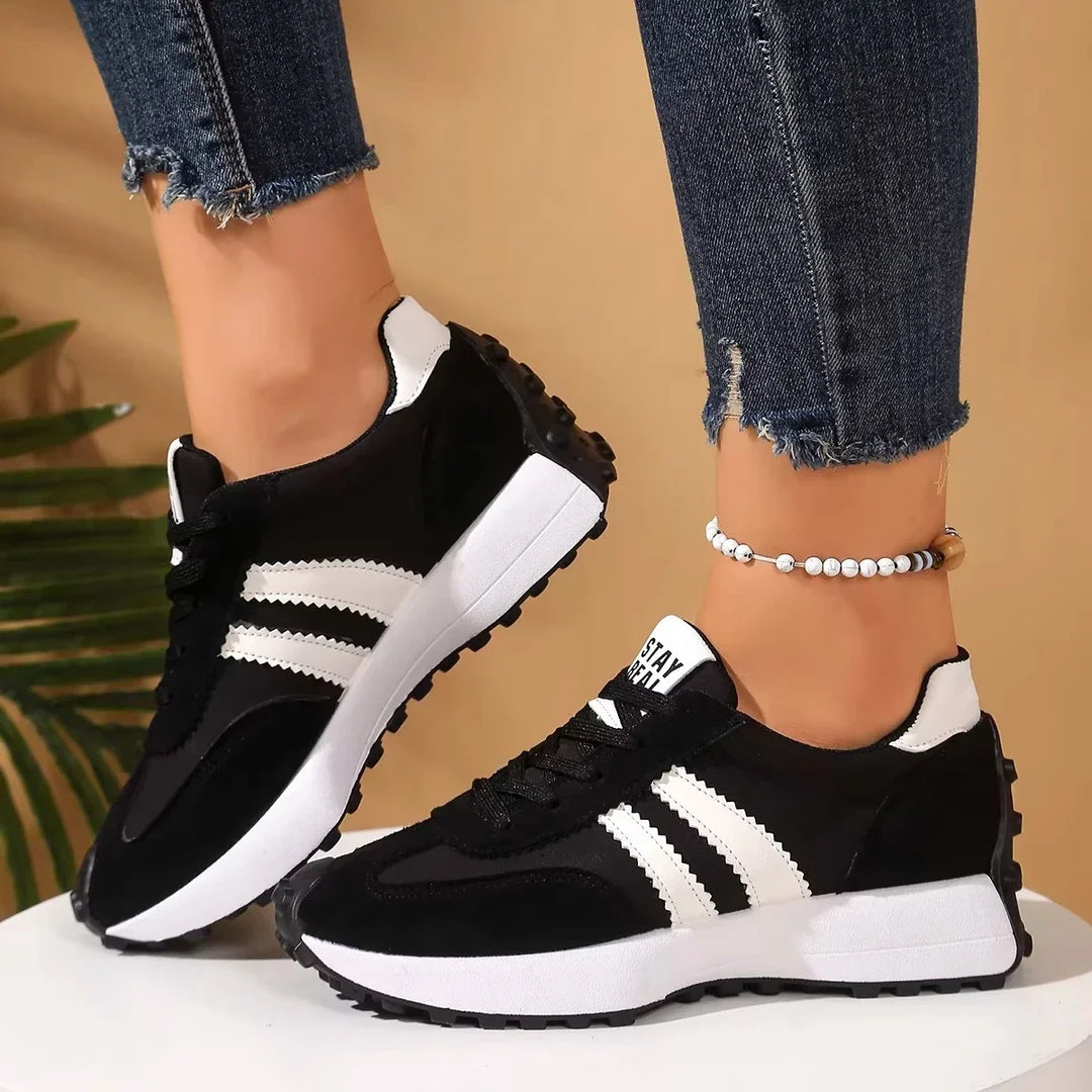 Side view of black platform trainers with white stripes and thick white midsoles, worn on a white pedestal 9