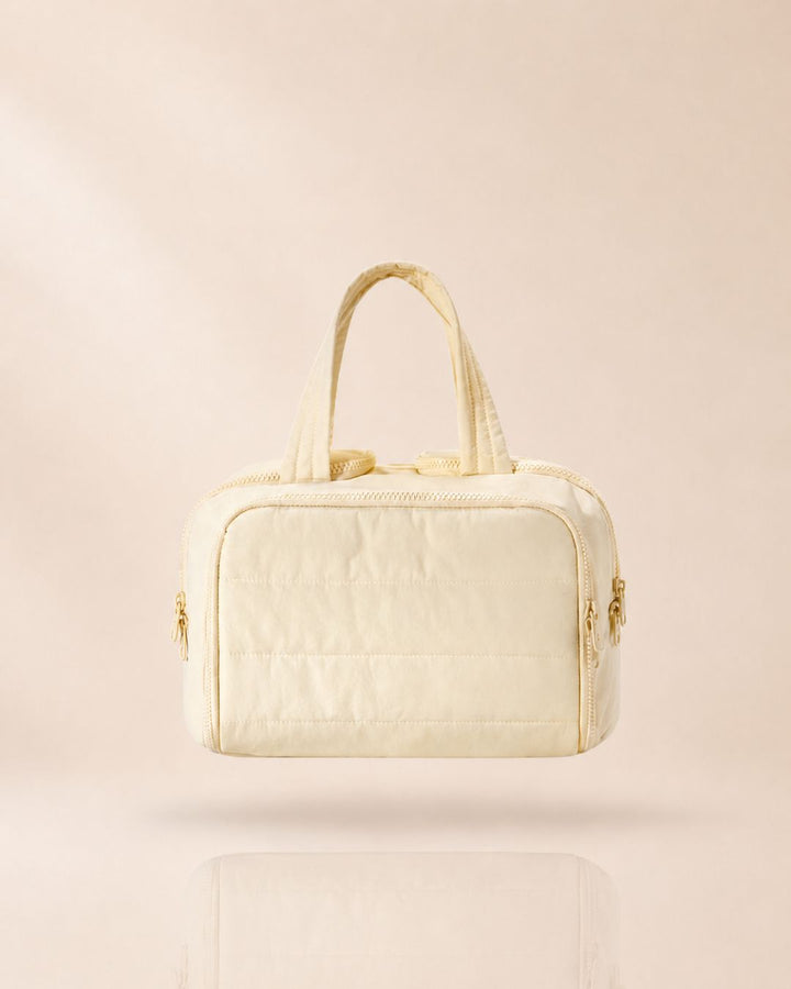 Cream-colored quilted bag with two handles, front view against a soft beige background.
