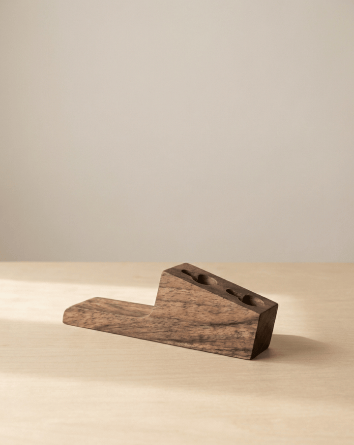 Single dark wood hook lying on a light tabletop, showing its angled wedge shape and two screw holes on the sloped face. 4