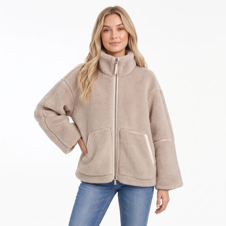 Model in a taupe fleece zip coat with cream pocket trim and one hand on her hip 9