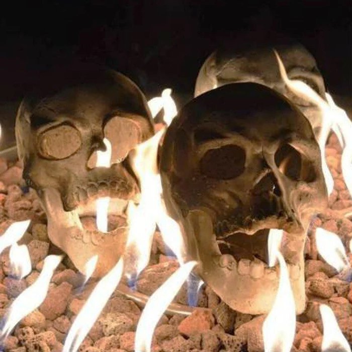 Detail of skulls on reddish lava rock with pale blue-white gas flames around their jaws and eye sockets.