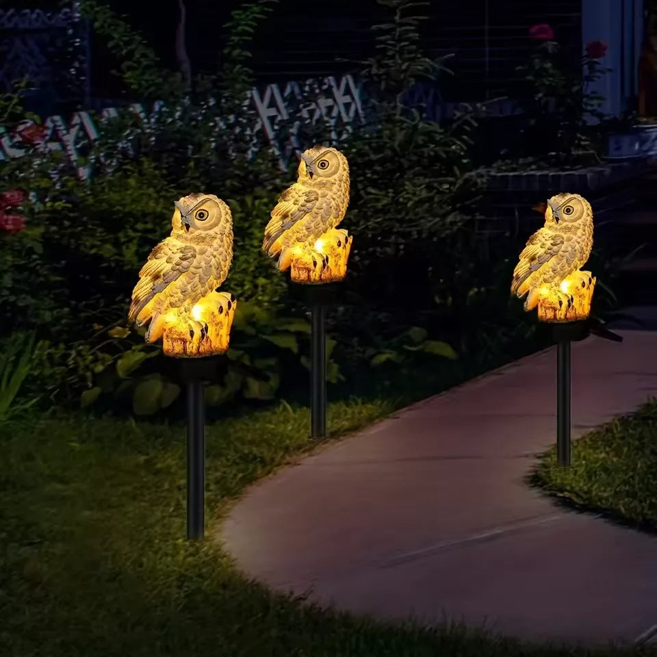 Three owl lights glowing amber along a curved garden path at night 9